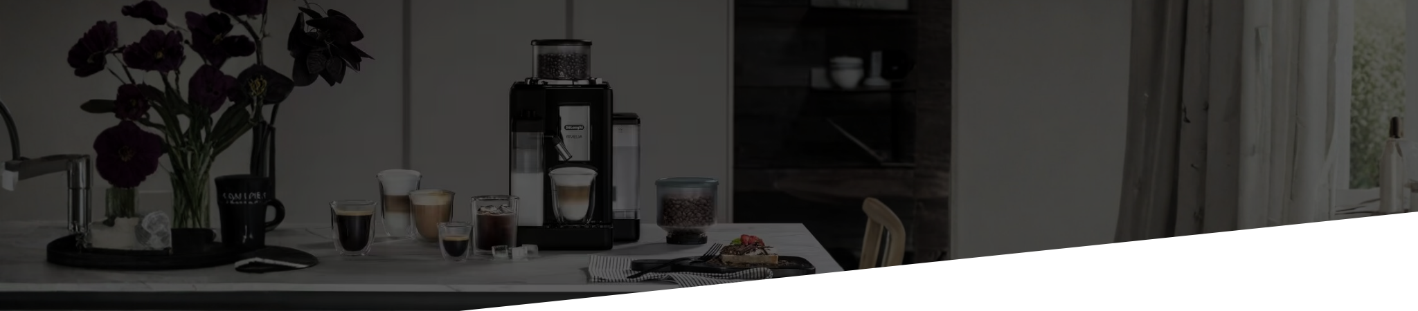 De'longhi Coffee-making setup with a coffee machine, cups, and flowers on a table.