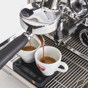 Espresso machine pouring coffee into two white cups with a visible brand logo.