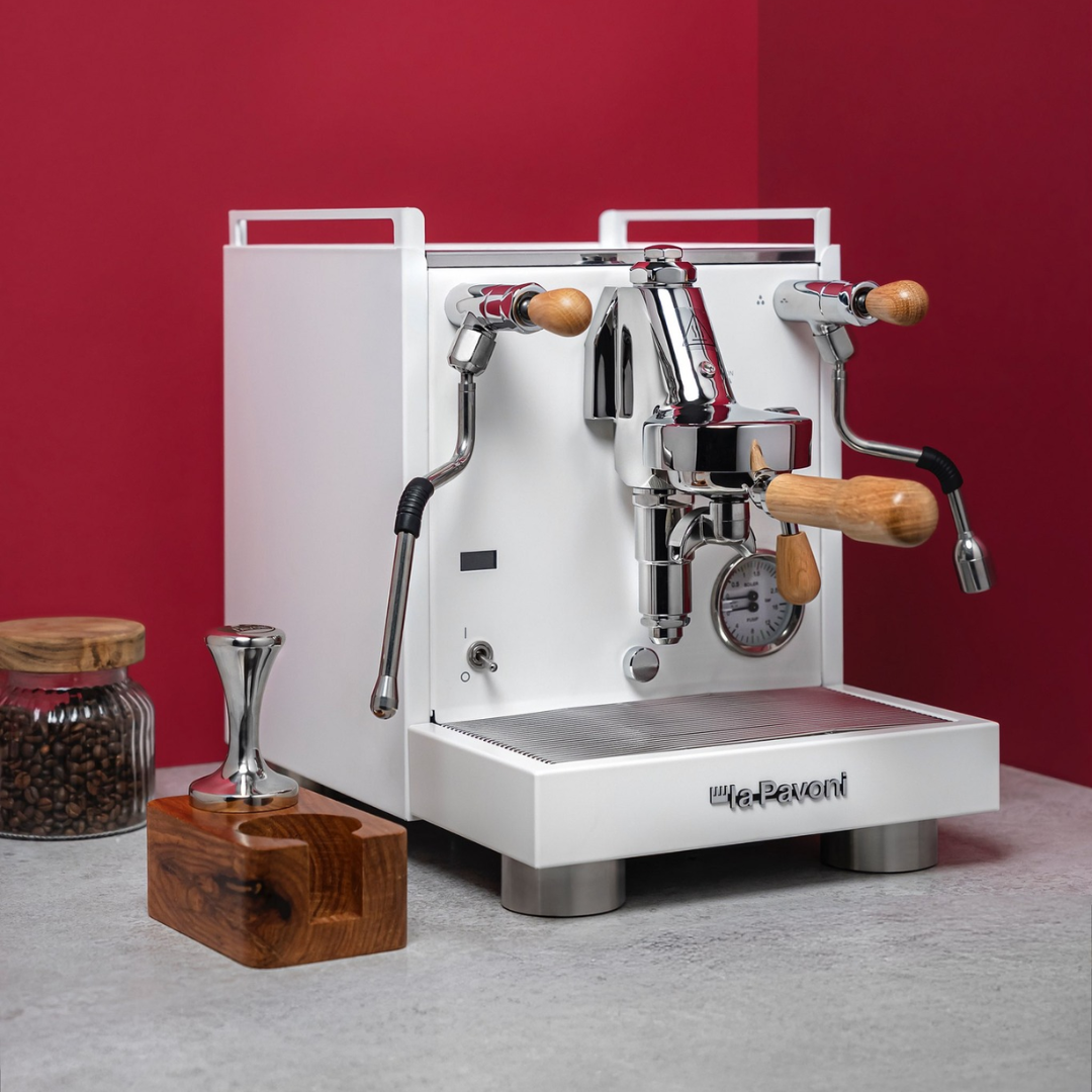 White espresso machine with wooden handles on a gray surface against a red wall.