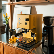 Yellow coffee machine on a kitchen bench top with warm lighting next to a coffee grinder. 